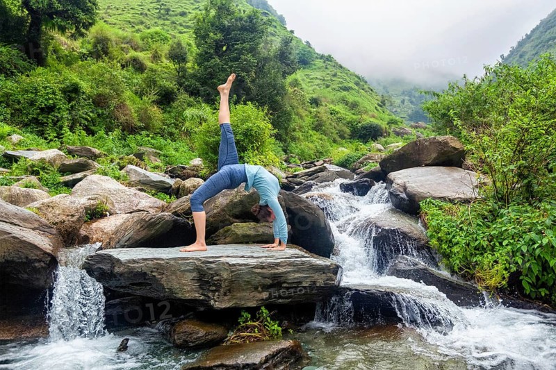 Yoga outdooors, woman doing yoga asana eka pada urdva dhanurasana Upward Bow Pose back benkd outdoors at waterfall in Himalayas