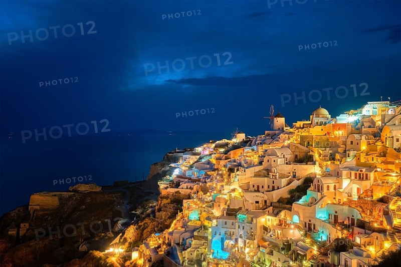 Famous greek iconic picturesque tourist destination Oia village with traditional white houses and windmills in Santorini island in the evening blue hour, Greece