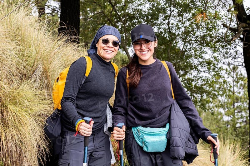 A cheerful pair of hikers take a break on a scenic forest trail. Dressed in outdoor gear and carrying backpacks, they embody the spirit of adventure and camaraderie in nature