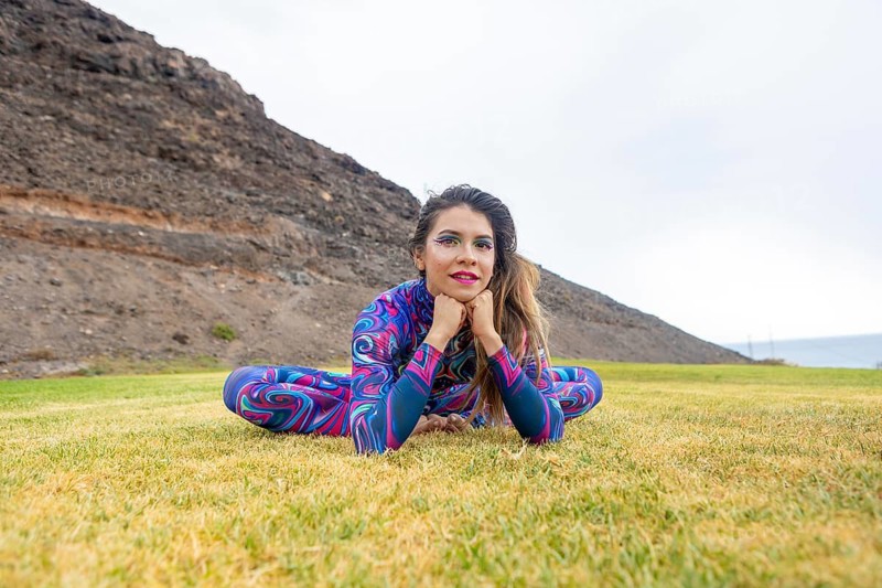 A woman in a vibrant, patterned costume poses gracefully on grass, symbolizing freedom and LGBTQIA+ pride. The natural backdrop enhances her confident expression