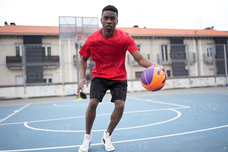Frontal full length photo of an african basketball player dribbling in an outdoor basketball court