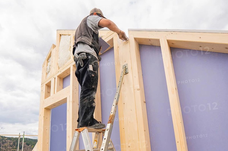 Man standing on ladder and working on timber frame construction under cloudy sky, residential building renovation, Nagold, Calw district, Germany