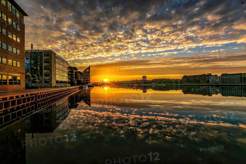 Farbintensiver Sonnenuntergang spiegelt sich im Wasser zwischen modernen Gebäuden, Kopenhagen, Dänemark