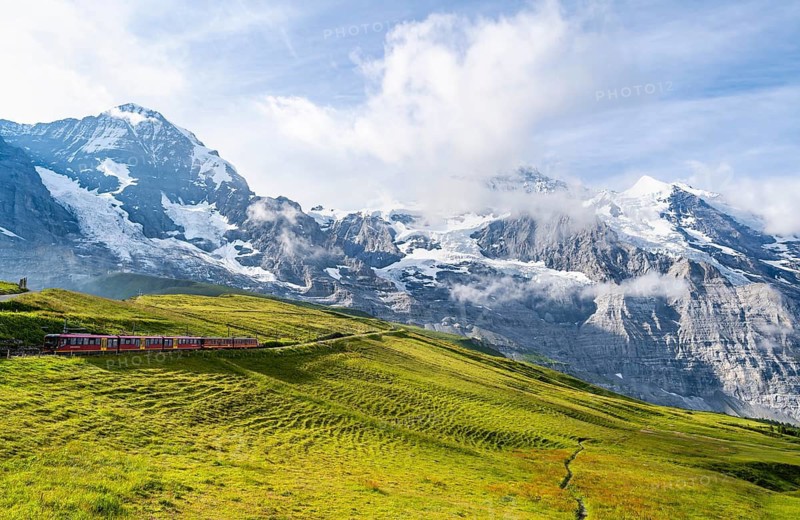 Jungfrau Railway to Jungfraujoch runs through green meadows, above the Kleine Scheidegg stop, rack railway, in the back mountains with peaks Eiger, Mönch and Jungfrau, Jungfrau region, Bernese Oberland, Switzerland