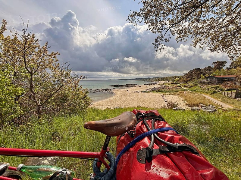 A bicycle stands on a hill overlooking a sandy beach and the sea under dramatic clouds, Allinge, Bornholm, Denmark