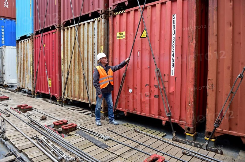 In port, a man pulls safety ropes on a tall container stack with protective clothing, workers on the tie rods on a container ship, Schleswig-Holstein, Germany