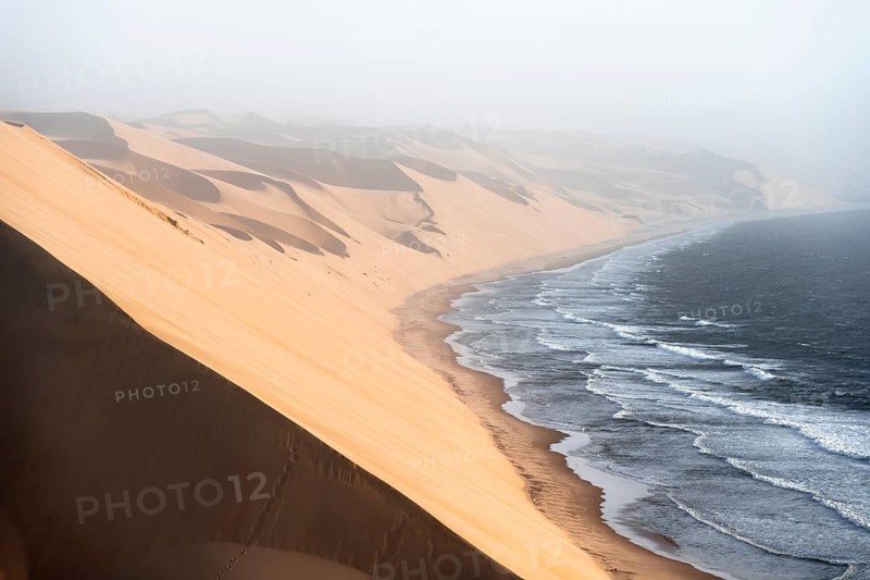 Sand dunes with wave patterns and sea in evening light, wind blowing sand across the dunes, Atlantic coast and sandy desert with sea of dunes, impressive desert landscape, Sandwich Harbour, Namib Naukluft Park, Namib Desert, Namibia