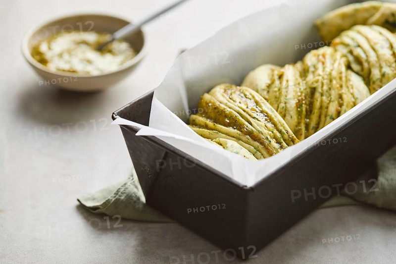 Ready to bake, homemade savoury babka plaited bread loaf flavoured with cheese and pesto, in the making tin