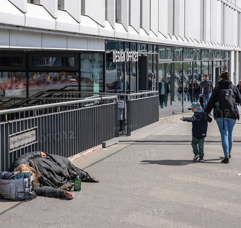 Little child holding mother's arm points at a sleeping homeless person, Hugo Preuß Brücke, Berlin, Germany