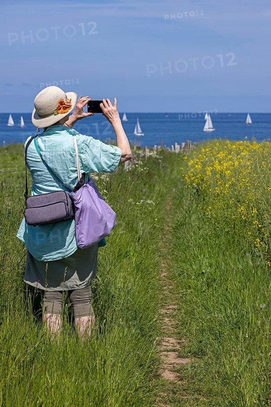 Woman taking pictures with smartphone, sailboats, rapeseed field, Baltic Sea, Altbülk, beaches, Schleswig-Holstein, Germany