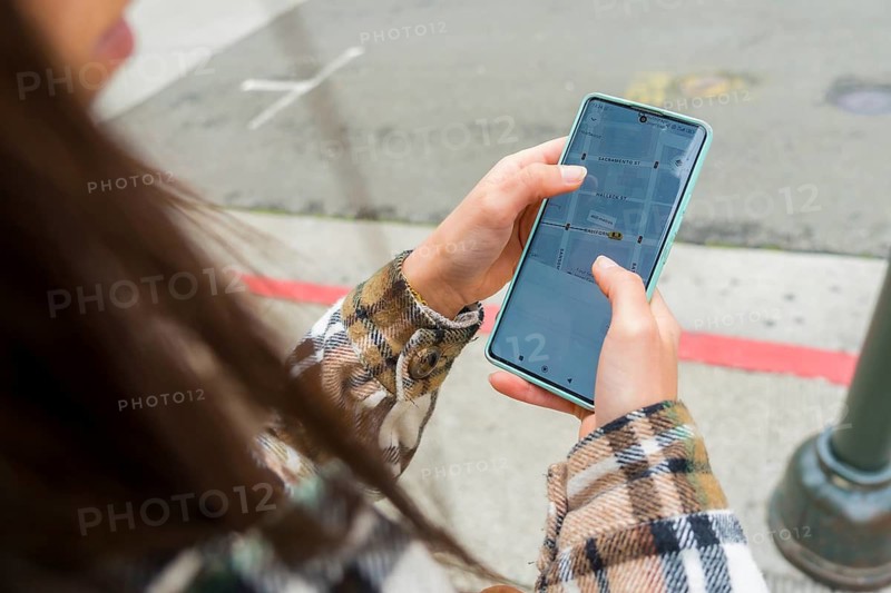 Woman standing on a san francisco street, holding a smartphone with a navigation map displaying streets and locations, actively using the device for urban wayfinding