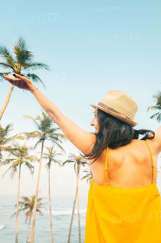 Carefree happy woman traveler in yellow summer dress and straw hat enjoy palm beach in tropical destination on holiday vacation. Tourism tour tropical travel vacation holidays. Palm tree backdrop