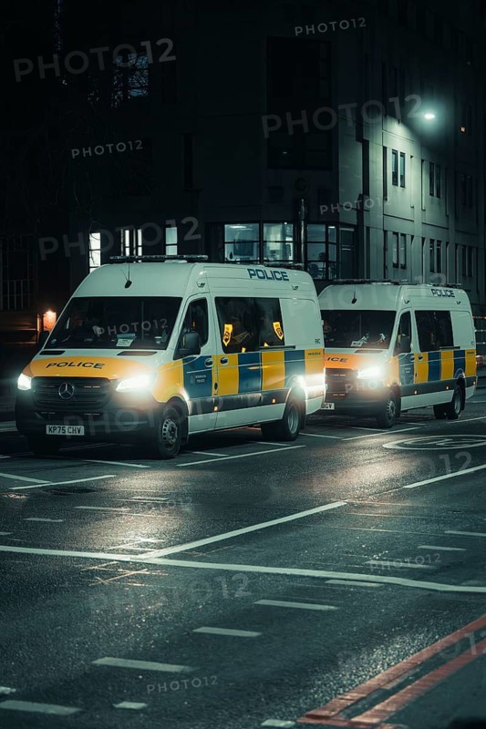 Two police vehicles on an illuminated street at night in an urban environment, New Year's Eve London, Great Britain