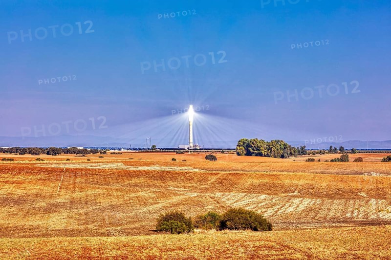 A solar tower rises above golden fields under a clear blue sky, solar thermal power plant PS10, Sanlúcar la Mayor, near Seville