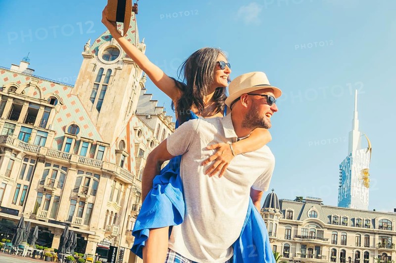 Beautiful young tourist couple having fun piggyback visiting Batumi Georgia. Tourists enjoying holiday in Europe in famous landmark - Vacation and happy lifestyle concept. Caucasus travel destination