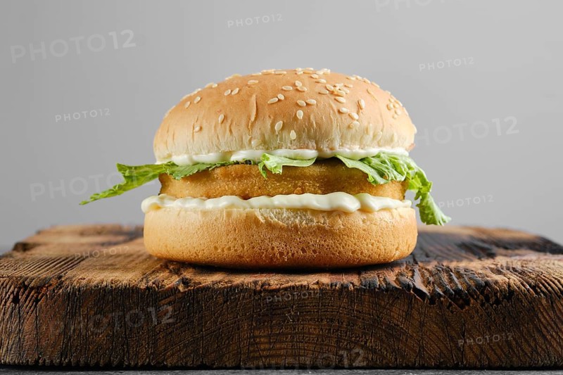 Chicken burger with fresh iceberg lettuce salad on wooden board, front view