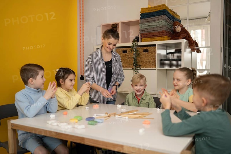 Children gather around a table for a creative lesson with a teacher. Smiling faces, bright colors, and arts materials create a joyful and educational atmosphere