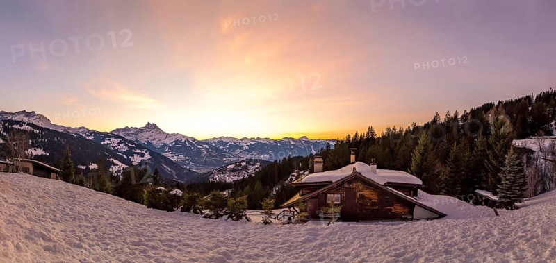 A stunning panoramic view of the Swiss Alps from Gryon, Vaud, showcasing the majestic Dents du Midi mountain as the sun sets, casting a warm glow over the snowy landscape