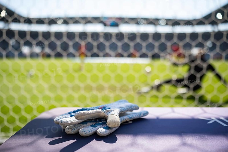 Goalkeeper's gloves lying behind the goal and soccer match in the background