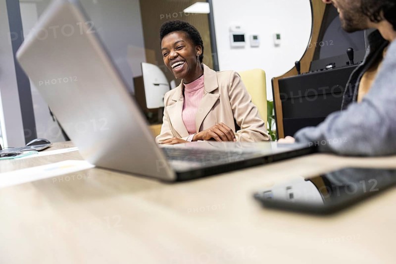 A lively and engaging office scene, showcasing smiling professionals collaborating in a modern workspace. The image captures teamwork, technology, and positive interaction