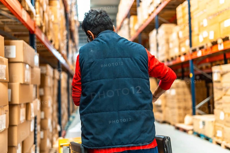 Rear view of a latin male worker pushing an hydraulic hand pallet truck on a warehouse