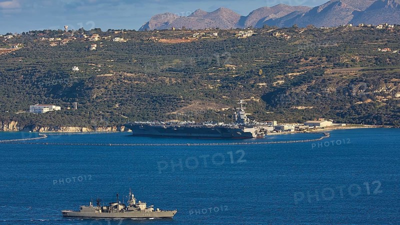 Aircraft carrier USS Gerald R. Ford, largest aircraft carrier in the world, anchored in Souda Bay on February 24, 2026, Greek Navy S-class frigate Kountouriotis, military ship and coastal strip with mountains in the background, US Navy, Souda Bay, Akrotiri Peninsula, Chania Province, Crete, Greek Islands, Greece
