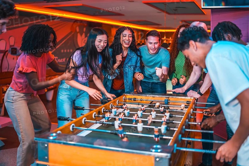 Young people enjoying vibrant moments together while playing table soccer in a lively entertainment venue filled with colorful lights