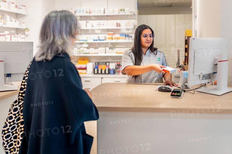 Saleswoman attending a woman in the counter of a pharmacy and checking the price of a medicine