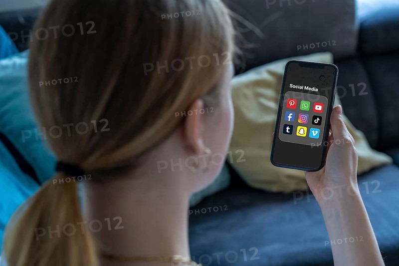 Symbolic image of social media use by young people, children, young woman, girl, 14 years old, folder with various social media platforms on the mobile phone