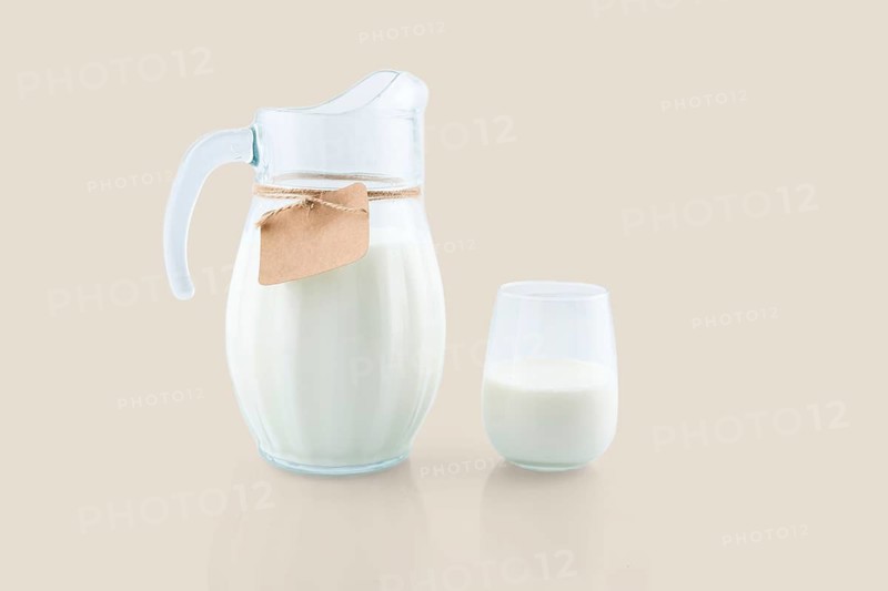 Fresh milk is being poured into a glass from a glass jug with a blank label attached