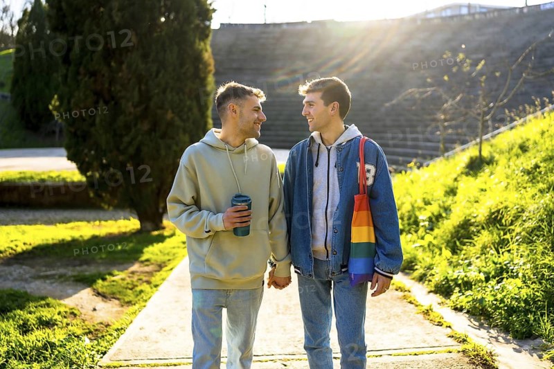 Happy caucasian gay couple holding hands and walking in a park, enjoying a sunny day together
