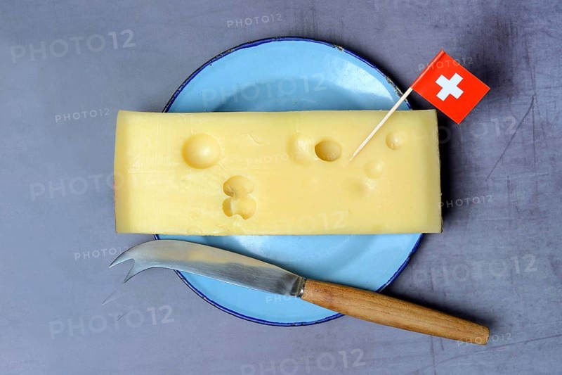 A piece of Swiss Emmental cheese on a plate and the Swiss flag