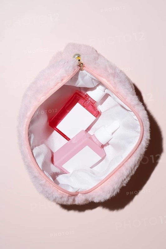A soft, pink fur cosmetic bag is open to reveal two vibrant skincare bottles with droppers. The image captures a stylish and inviting beauty accessory