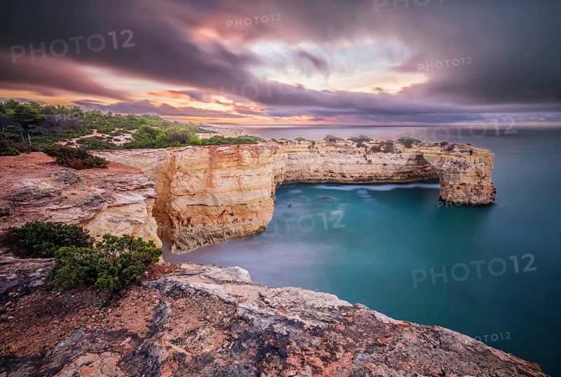 Long exposure sunrise at Praia de Albandeira beach in Algarve, Portugal, with Arco de Albandeira, smooth ocean water and dramatic clouds. Long exposure