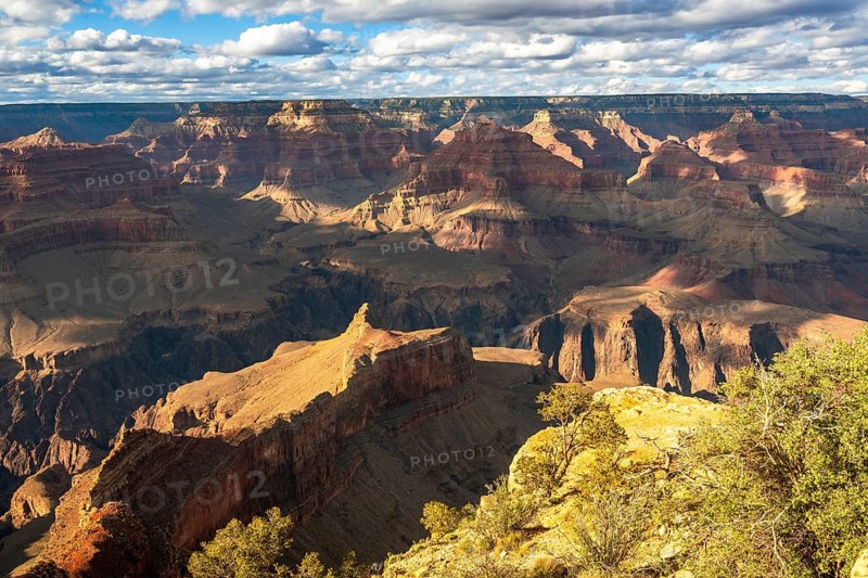 Grand canyon national park vista showing layered red rock formations and a deep sunlit gorge under scattered clouds, dramatic light revealing rugged, remote desert topography