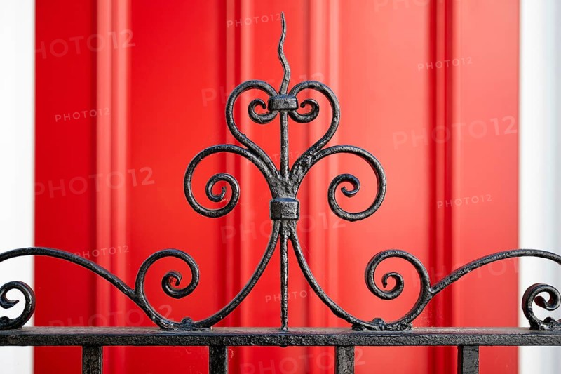 Close-up of an elegant curved metal grid in the foreground and red door in the background, Chelsea, London, Great Britain, England, Great Britain