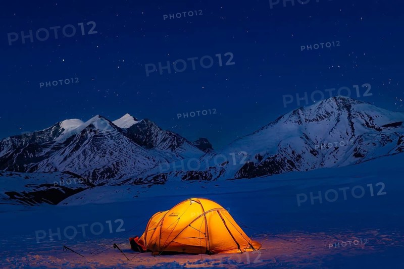 Illuminated tent in snow against snow-covered mountains and starry sky in Hidden Valley, plateau at 5100 m between French Pass and Dhampus Pass, Dhaulagiri Trekking, Dhaulagiri Himal, Himalayas, Nepal