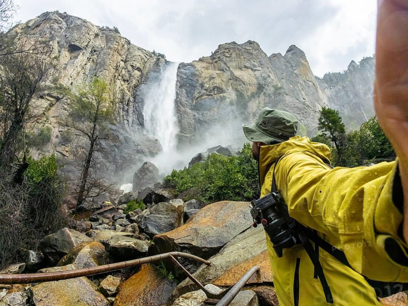 Hiker in a yellow jacket and hat is capturing the powerful flow of bridalveil fall, surrounded by the granite cliffs and natural beauty of yosemite national park in california