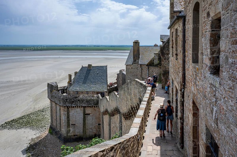 Tourists on the historic rampart of the medieval fortress wall on Mont-Saint-Michel at low tide with a view of the Wadden Sea, tourist attraction, UNESCO World Heritage Site, Pontorson, Manche department, Normandy, France