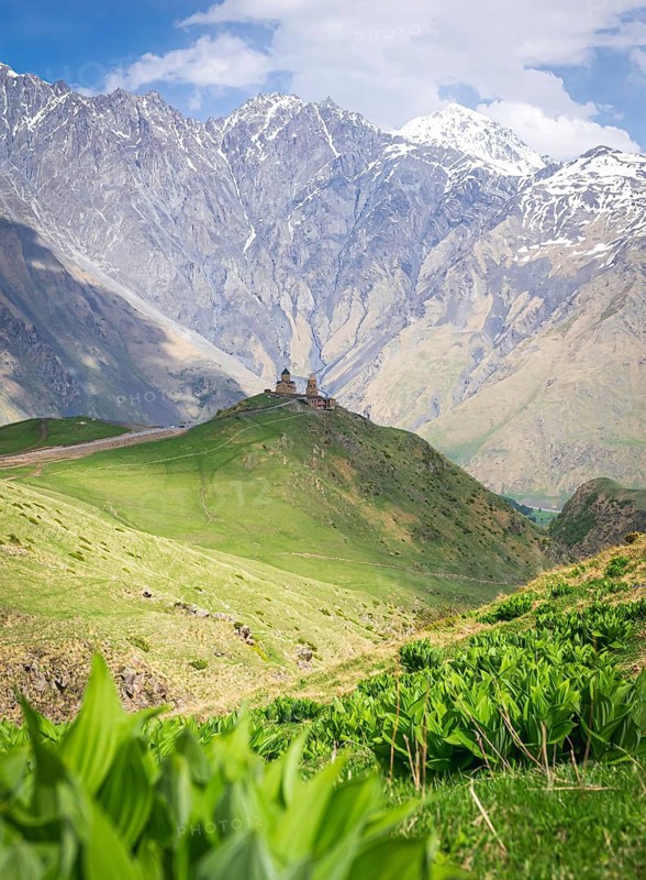 Historical Gergeti trinity church on top of the hill surounded by green nature and mountain in the background. Travelous in KAzbegi national park. Georgia
