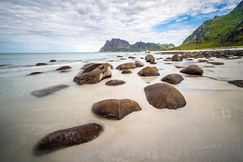 Rocks on Uttakleiv sandy beach, coast and blue sea, long exposure, rocky mountain peaks, Vestvågøya, Lofoten, Nordland, Norway