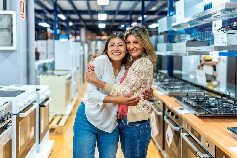 Happy mother and daughter smiling and hugging each other in a retail store, browsing kitchen appliances and home improvement items for their new house renovation project
