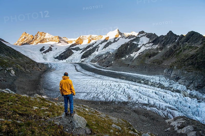 Young man in front of impressive high-alpine landscape, Finsteraarhorn and Agassizhorn mountain peaks with alpine glow at sunrise, Upper Arctic Ocean glacier, Bernese Alps, Bernese Oberland, Switzerland