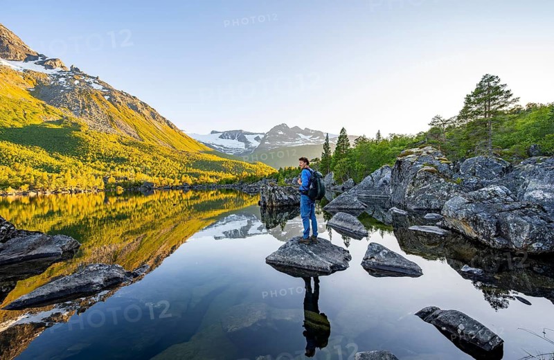 Young man enjoying the landscape, picturesque mountain scenery in the Innerdalen high valley, mountain peaks reflected in Lake Innerdalsvatna, in the evening light at sunset, Trollheimen Mountain Area, Sunndal, Møre og Romsdal, Norway