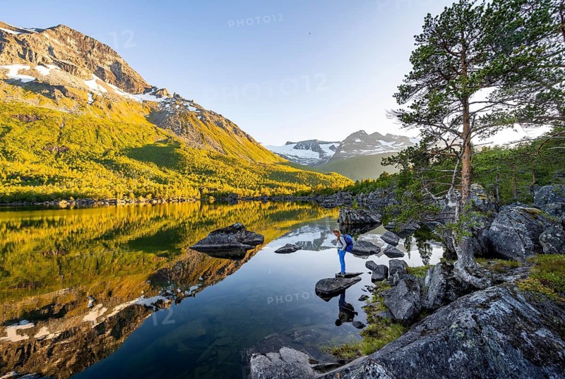 Young woman enjoying the landscape, picturesque mountain scenery in the Innerdalen high valley, mountain peaks reflected in Lake Innerdalsvatna, in the evening light at sunset, Trollheimen Mountain Area, Sunndal, Møre og Romsdal, Norway