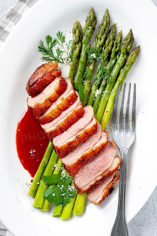 Roast duck breast, with asparagus, with red sauce, on a white plate, homemade, no people