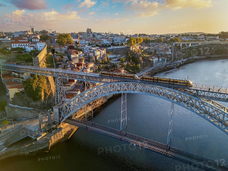 Drone view of Dom Luis I Bridge over Douro River in Porto, Portugal, with the riverfront, including a tram on the bridge at sunrise