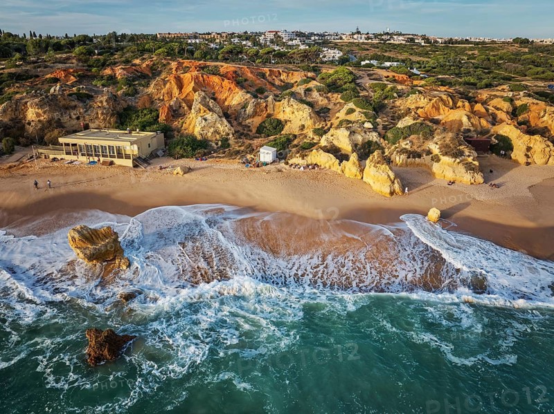 Drone view of waves curling along the beach below golden limestone cliffs at Praia de Sao Rafael beach