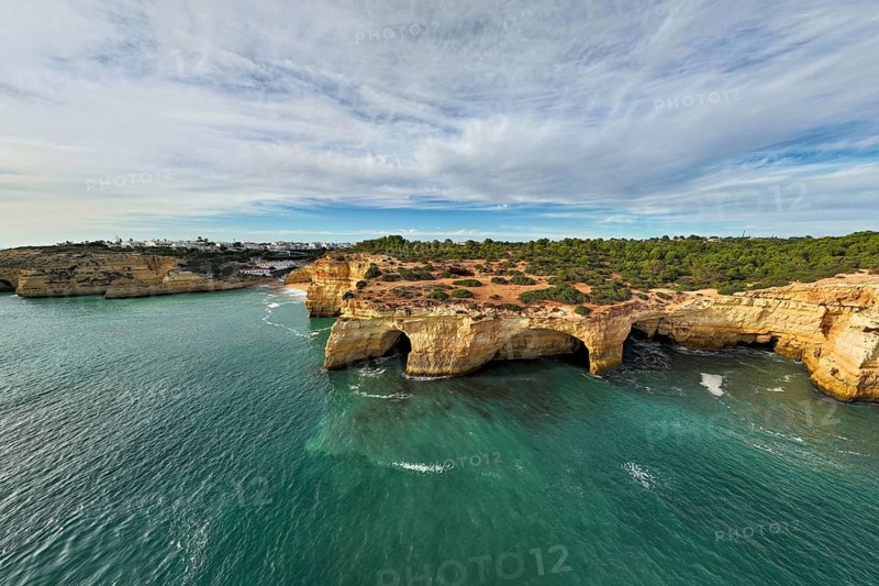 Drone view of cliffs above Benagil Cave in Algarve, Portugal, with limestone sea caves, turquoise Atlantic water, waves, and rugged coast