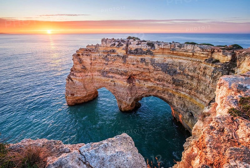 Sunrise at Praia da Marinha beach in Algarve, Portugal, with ocean cliffs, sea stacks and bright clouds over the sea